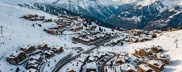 Vue aérienne panoramique du domaine de Courchevel en hiver montrant les quatre stations (1300, 1550, 1650 et 1850) étagées sur les pentes enneigées avec les chalets, les pistes de ski et les sommets des 3 Vallées en arrière-plan sous une lumière dorée de fin d'après-midi